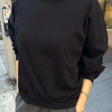 Person wearing a black sweatshirt with a red collar on a city street.