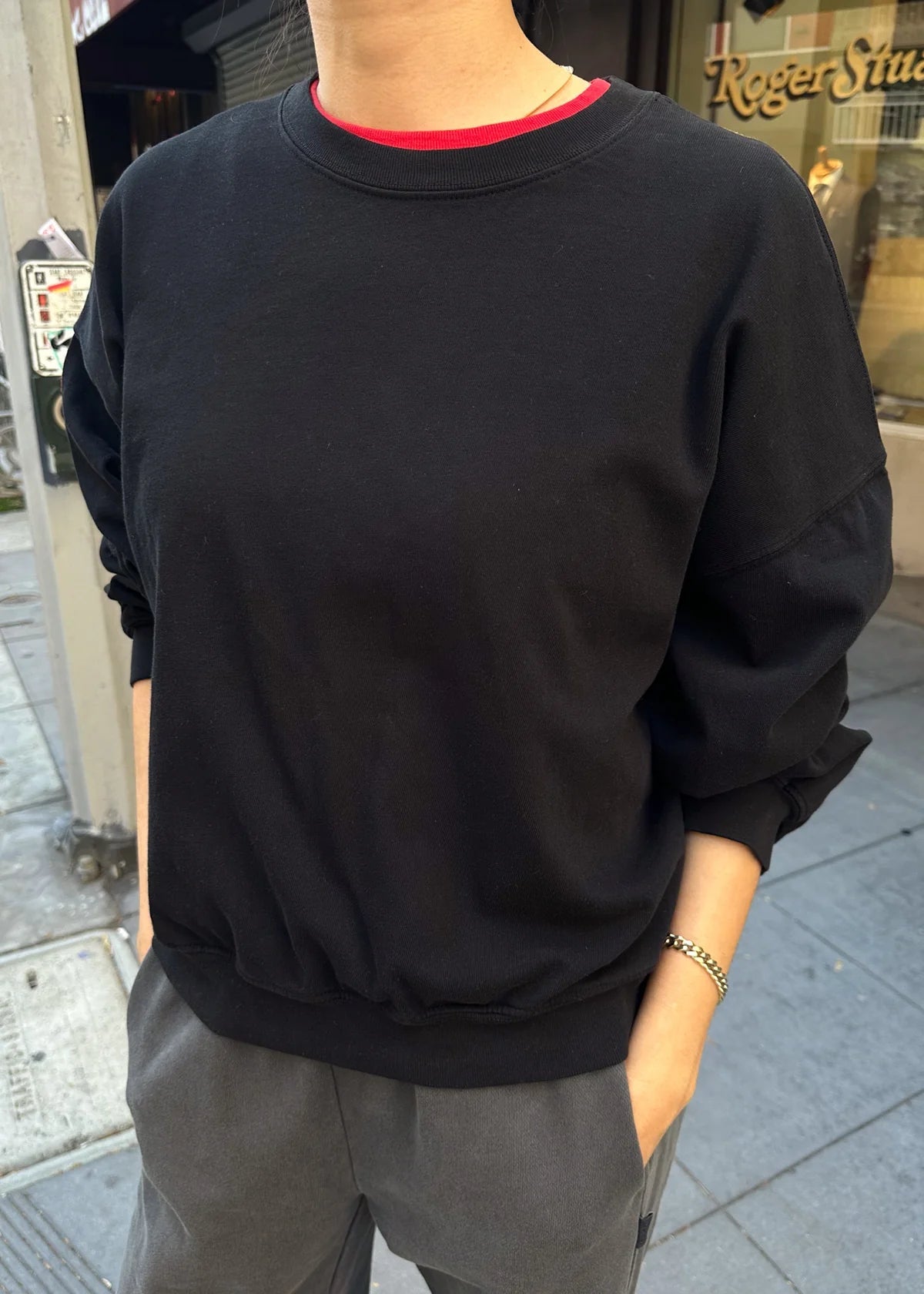 Person wearing a black sweatshirt with a red collar on a city street.