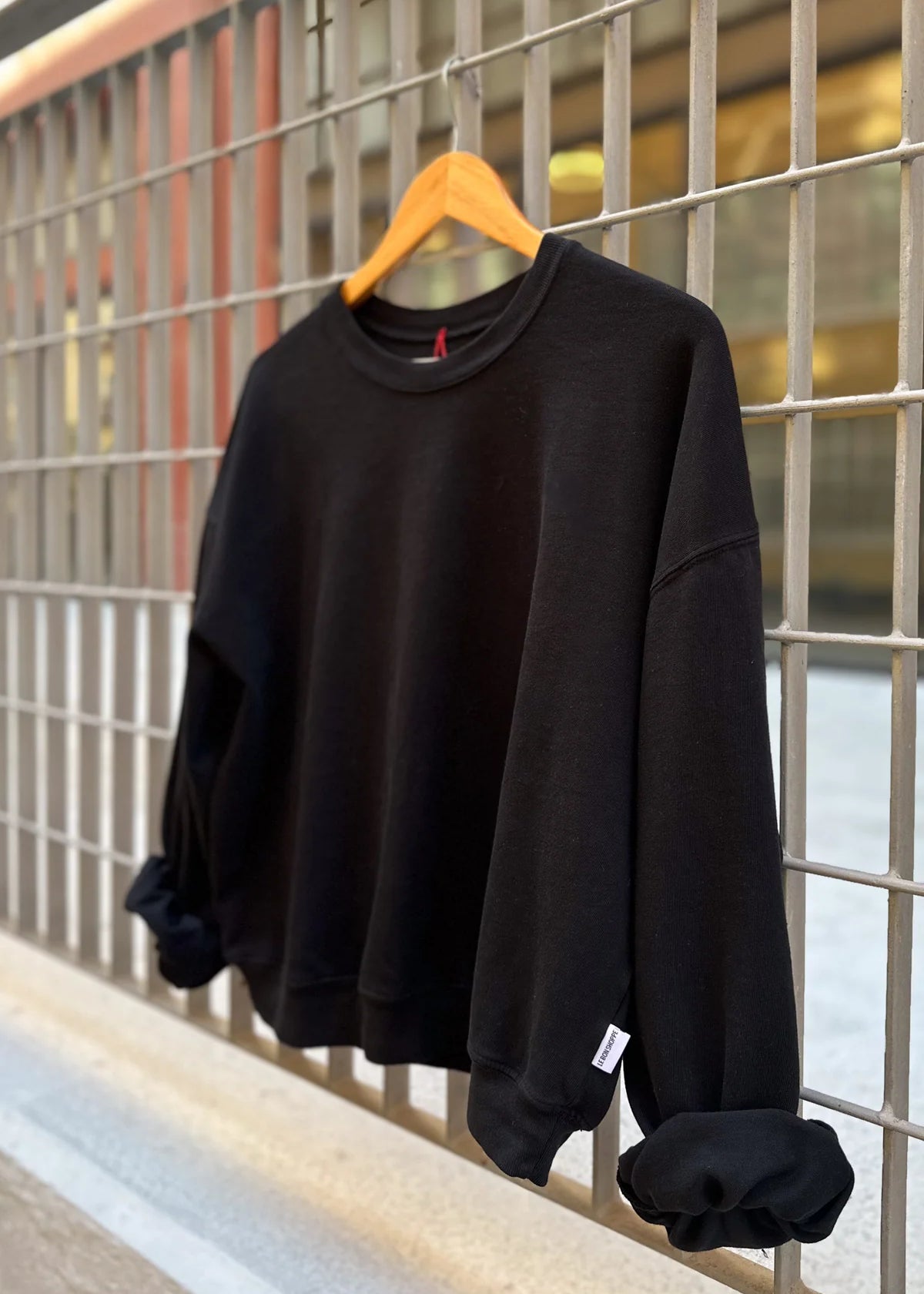 Black sweatshirt on a wooden hanger against a metal grid background