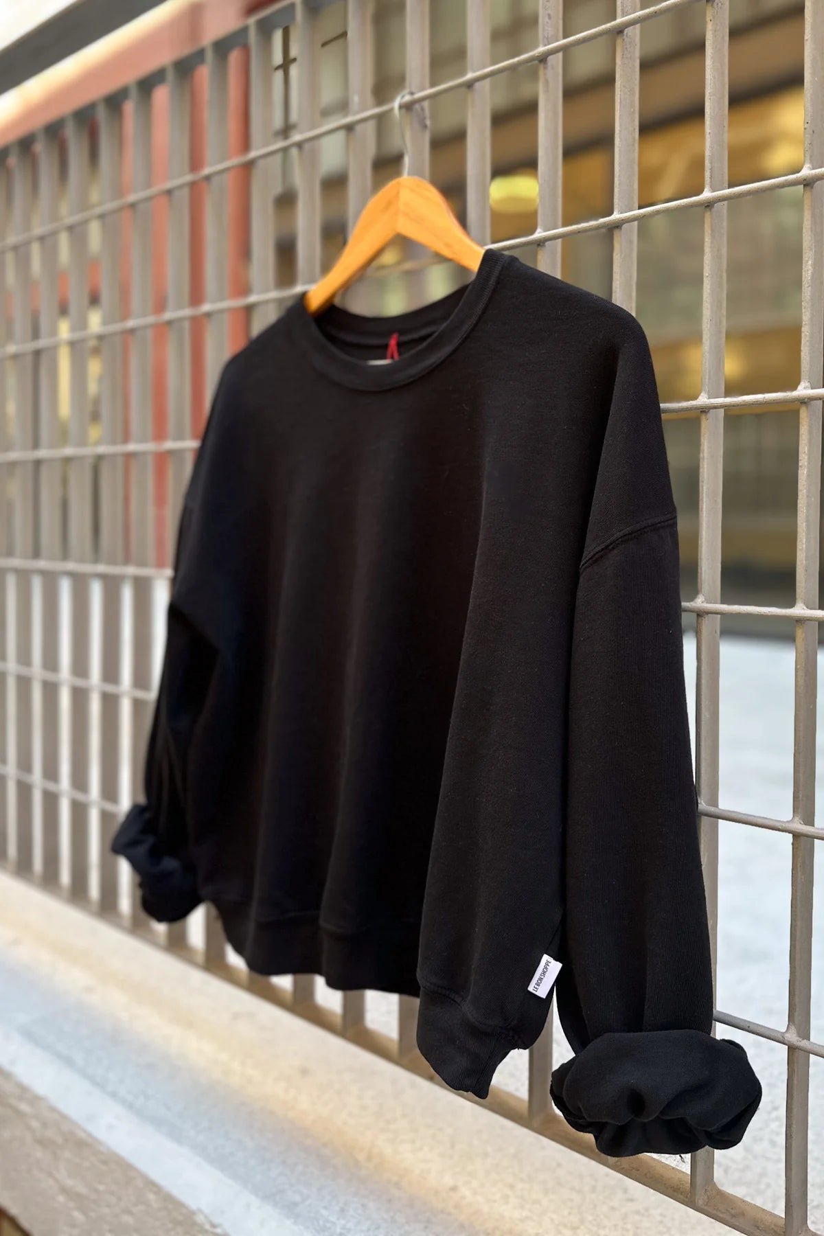 Black sweatshirt on a wooden hanger against a metal grid background