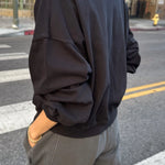 Person wearing a black sweatshirt and gray pants on a city street.
