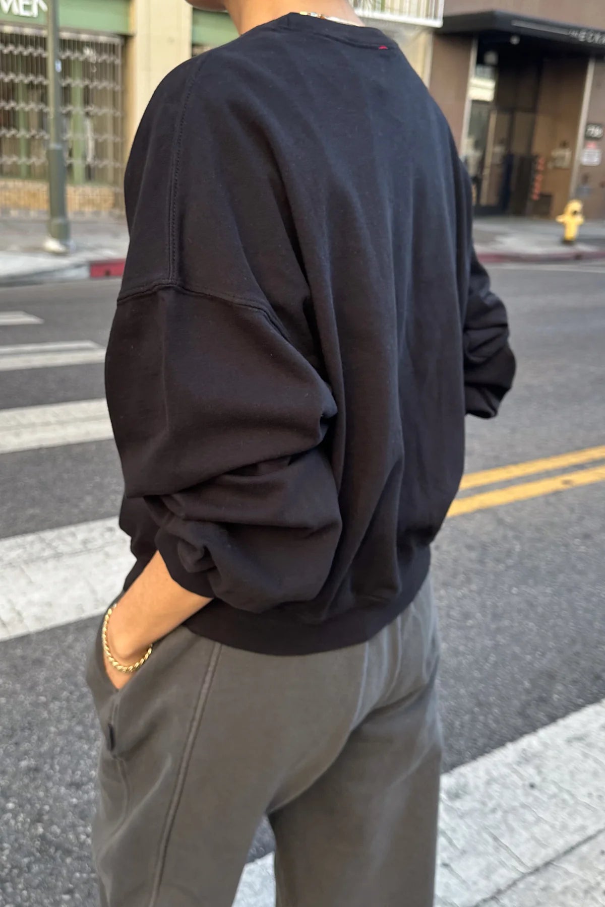 Person wearing a black sweatshirt and gray pants on a city street.