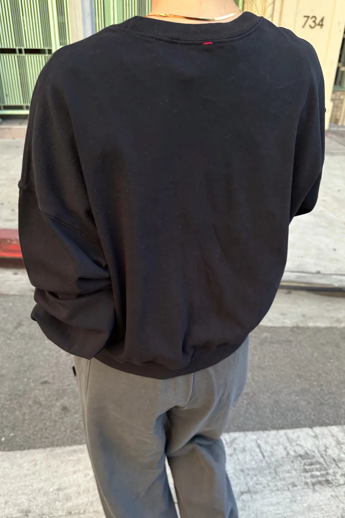 Person wearing a black sweatshirt and light gray pants on a street.