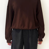 Person wearing a brown sweatshirt and dark pants against a white background