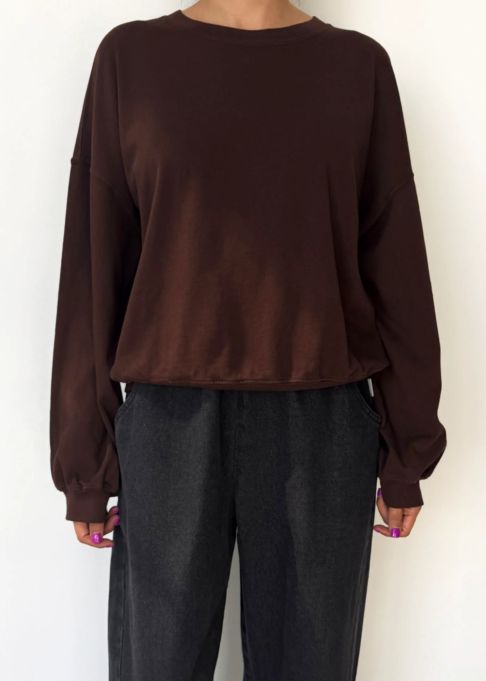 Person wearing a brown sweatshirt and dark pants against a white background