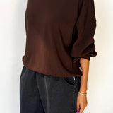 Person wearing a brown oversized sweater and dark jeans against a white background