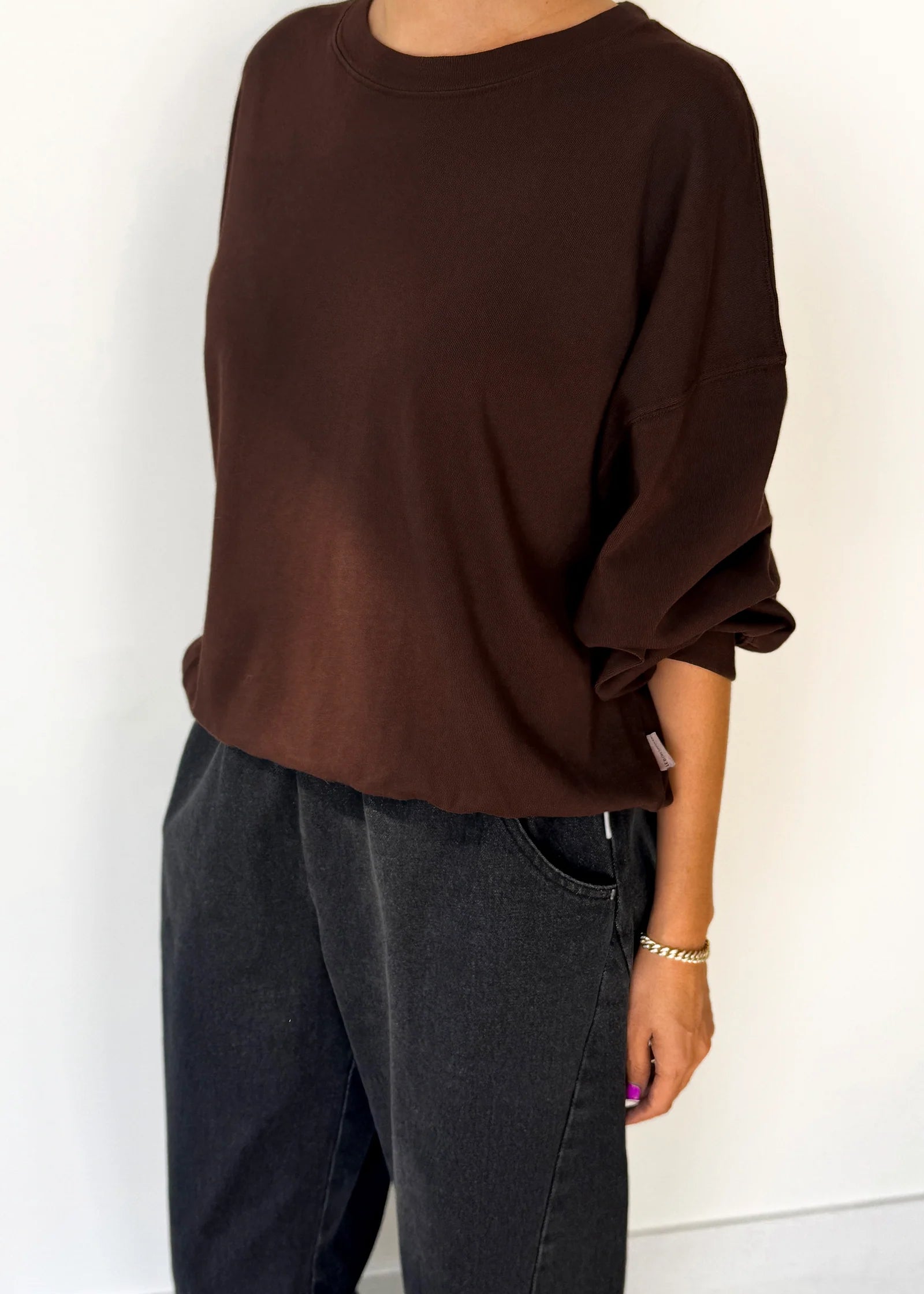 Person wearing a brown oversized sweater and dark jeans against a white background