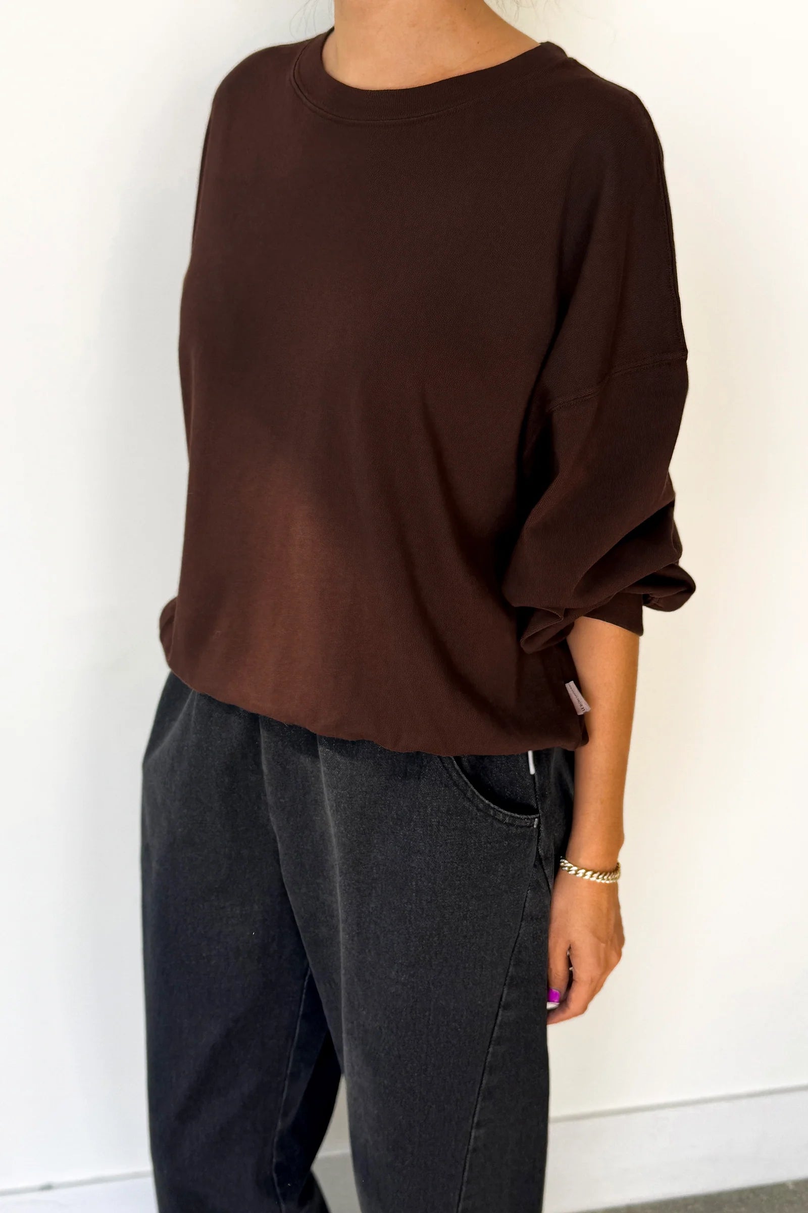 Person wearing a brown oversized sweater and dark jeans against a white background