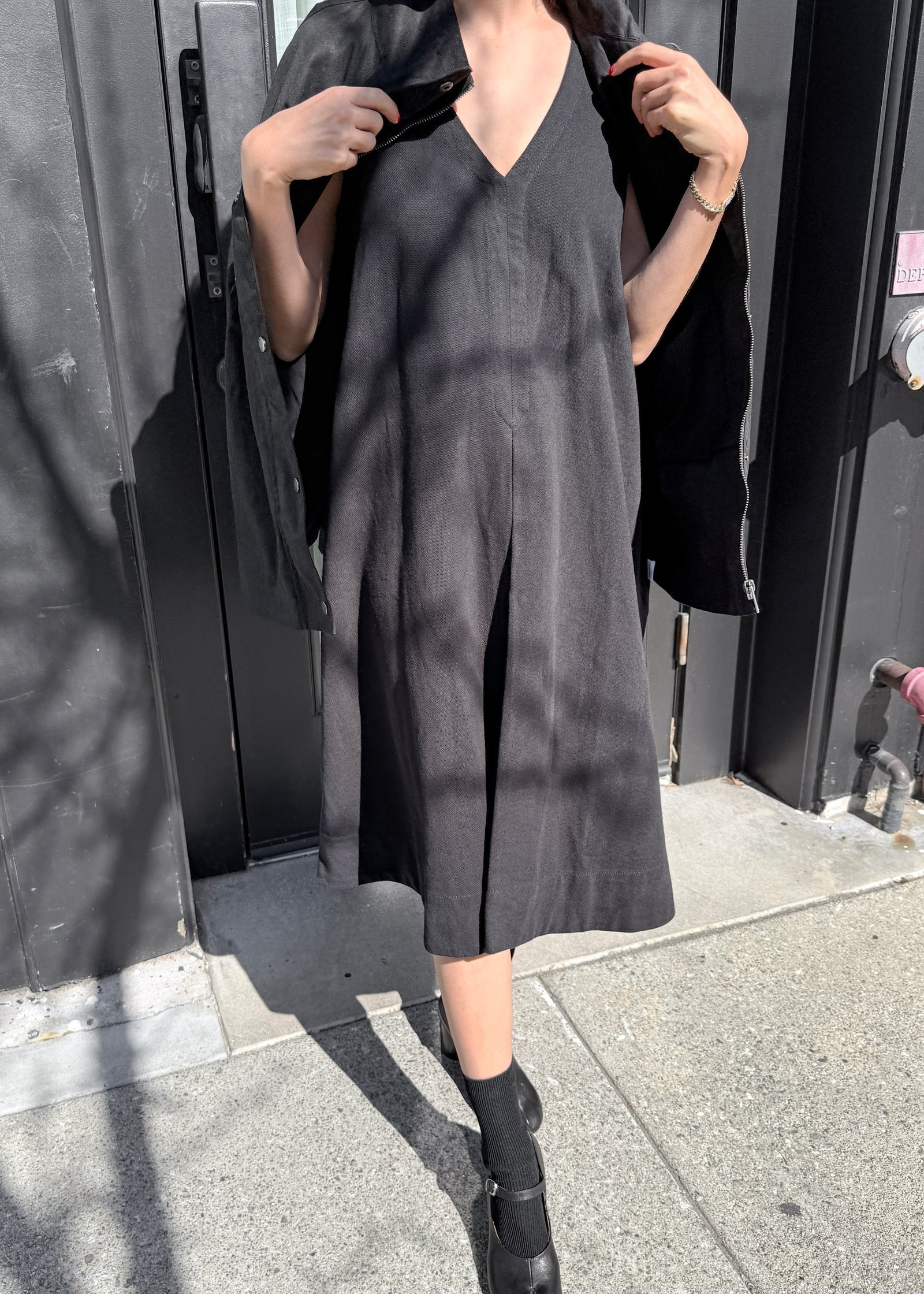 Person wearing a black dress standing against a dark background