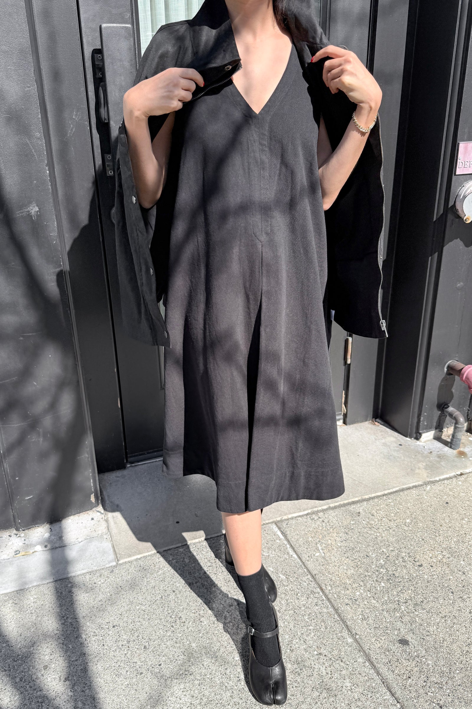 Person wearing a black dress standing against a dark background