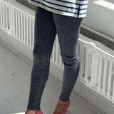 Person wearing a striped shirt, dark leggings, and pink shoes in a minimal indoor setting.