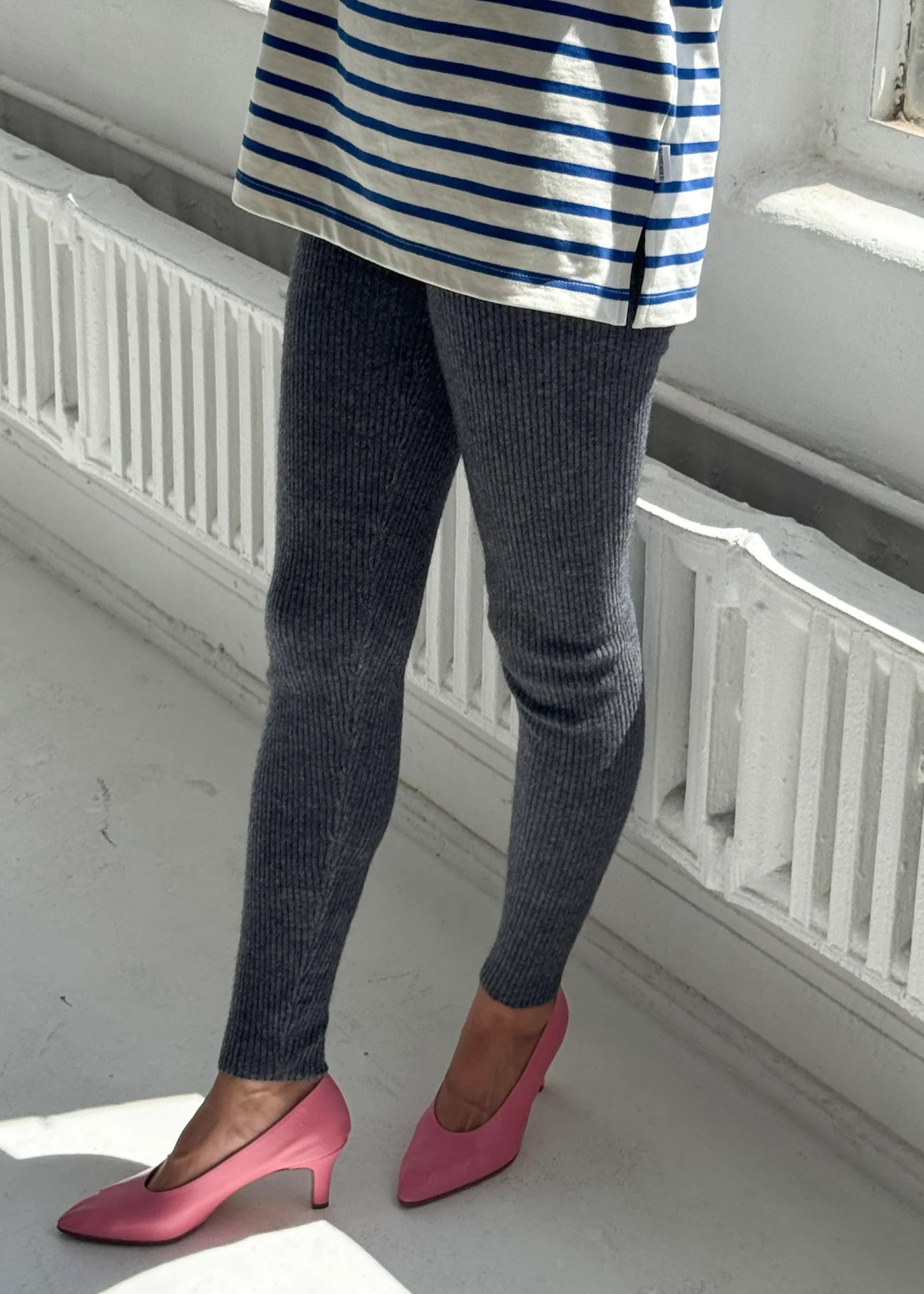Person wearing a striped shirt, dark leggings, and pink shoes in a minimal indoor setting.