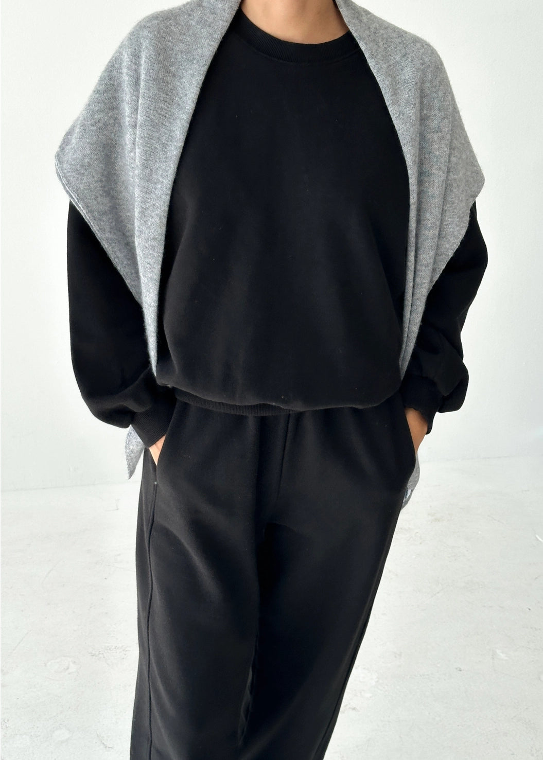 Person wearing a black outfit with a gray cardigan on a white background