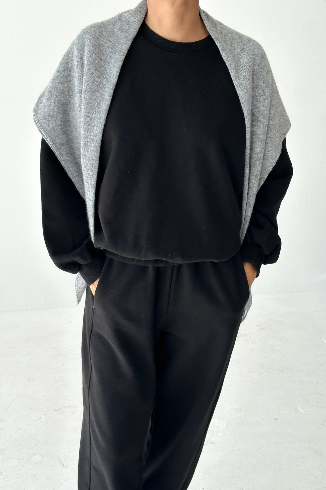 Person wearing a black outfit with a gray cardigan on a white background