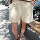 Person wearing a striped sweater and beige shorts standing on a sidewalk.
