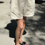 Person wearing white shorts and black sandals on a street.