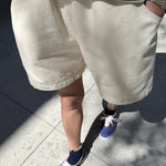 Person wearing a green and white striped shirt, beige shorts, and blue sneakers on a concrete surface.