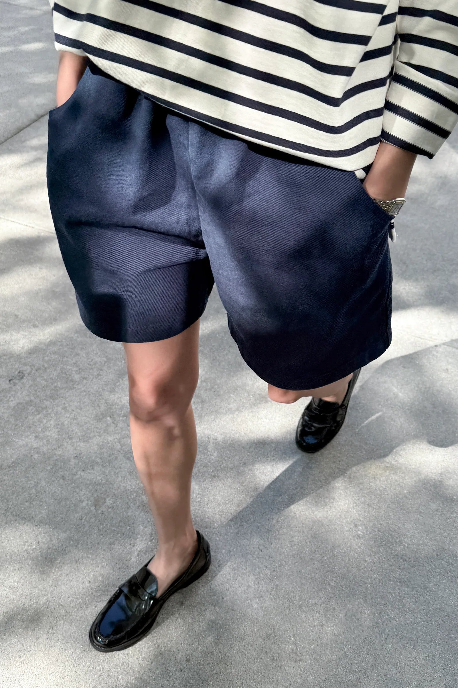 Person wearing navy shorts and a striped shirt on a concrete surface