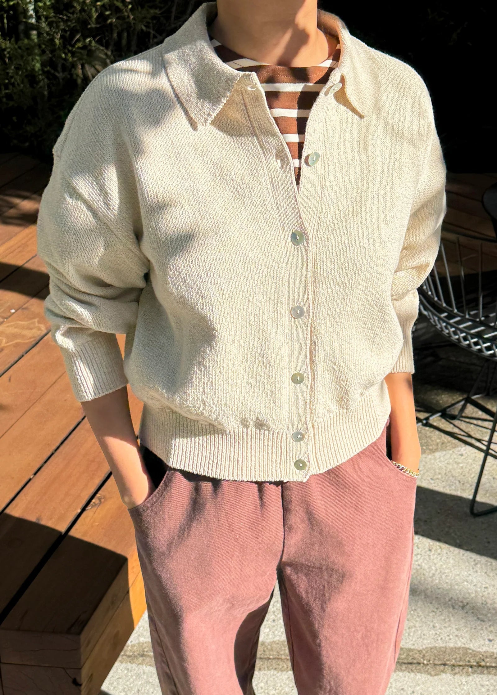 Person wearing a light-colored cardigan and pink pants outdoors.