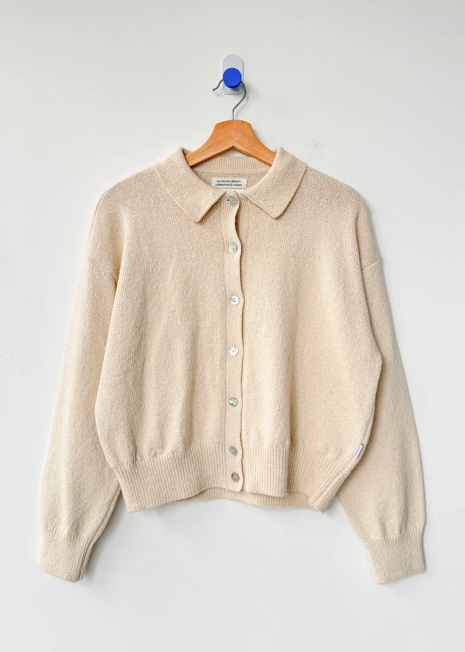 Beige cardigan on a wooden hanger against a white background