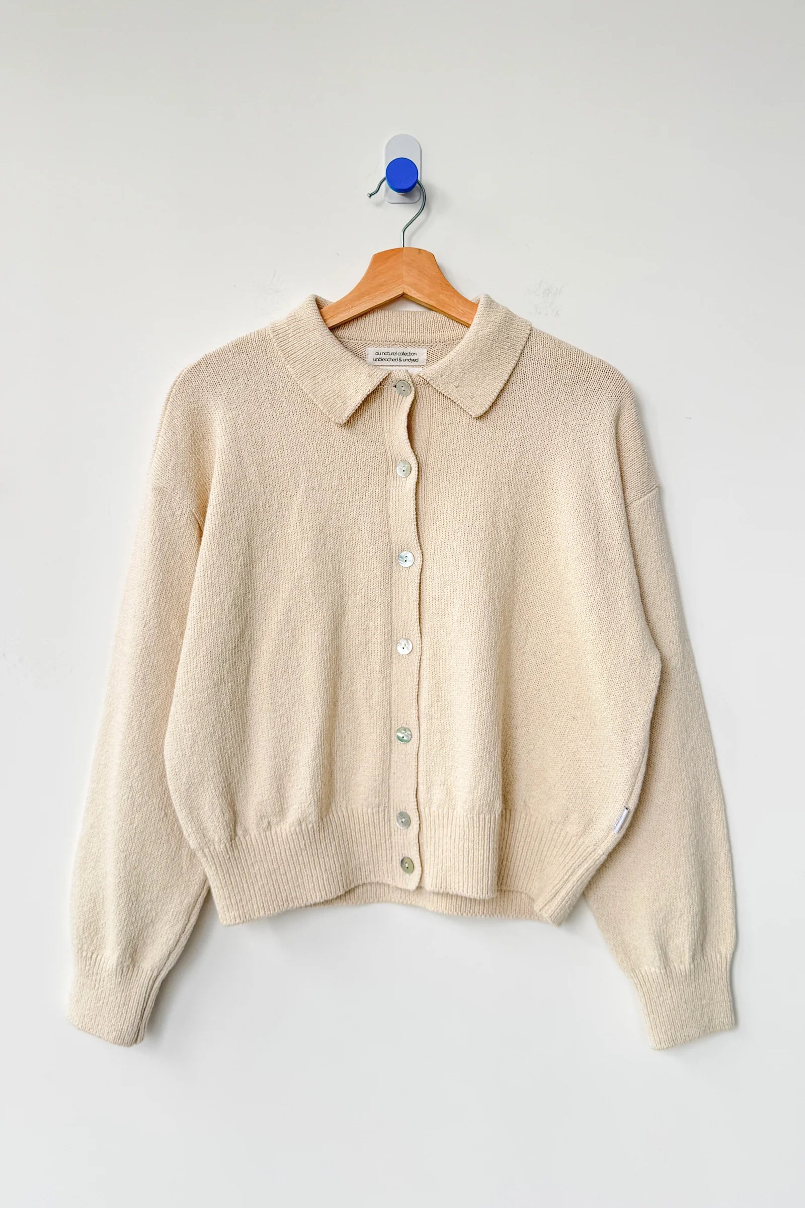 Beige cardigan on a wooden hanger against a white background