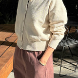 Person wearing a light-colored cardigan and brown pants outdoors.
