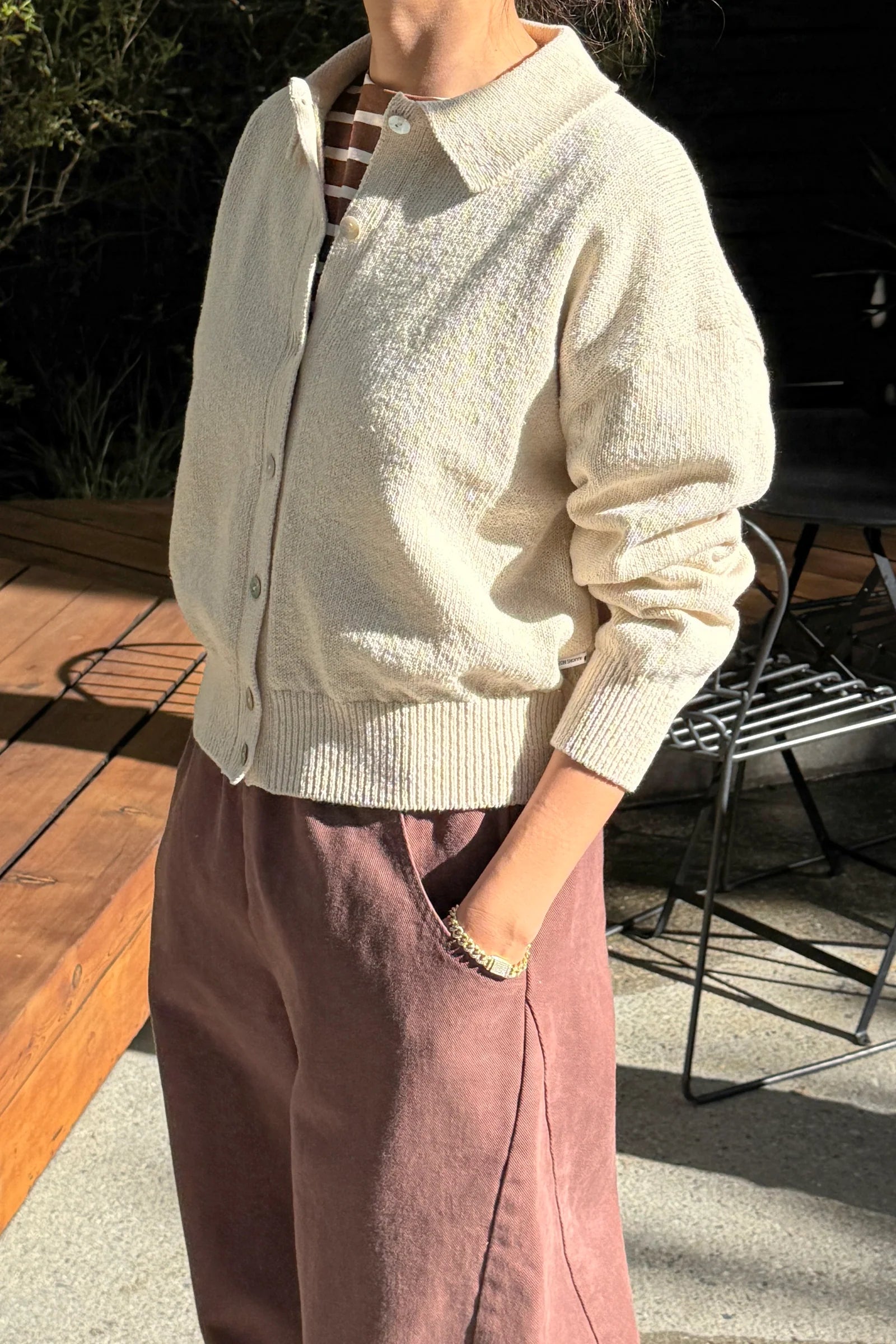Person wearing a light-colored cardigan and brown pants outdoors.