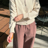 Person wearing a light-colored shirt and pink pants outdoors on a wooden deck.