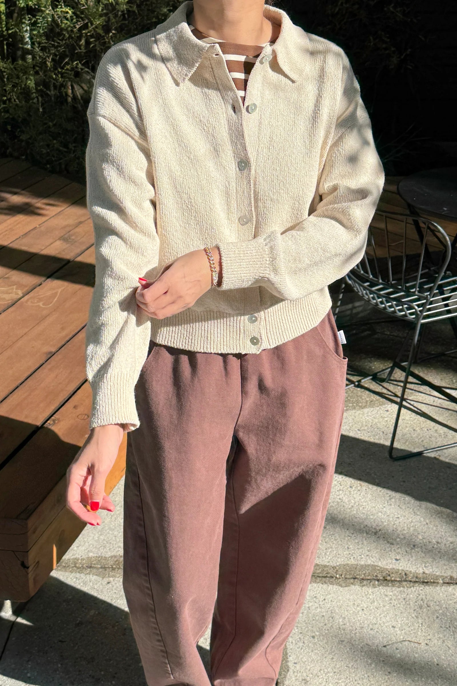 Person wearing a light-colored shirt and pink pants outdoors on a wooden deck.