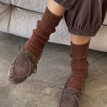 Person wearing brown moccasins and ribbed socks on a stone floor.
