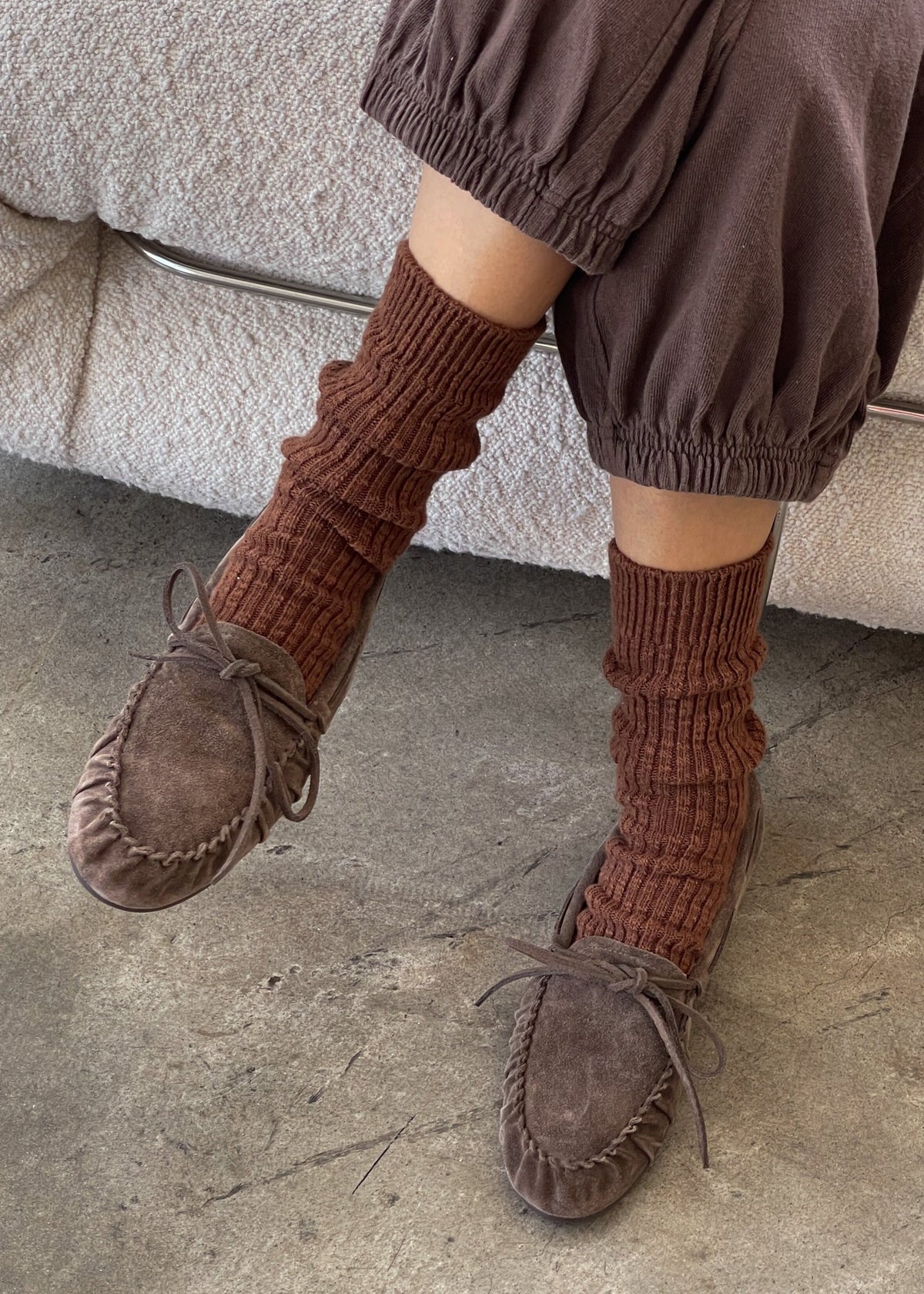 Person wearing brown moccasins and ribbed socks on a stone floor.