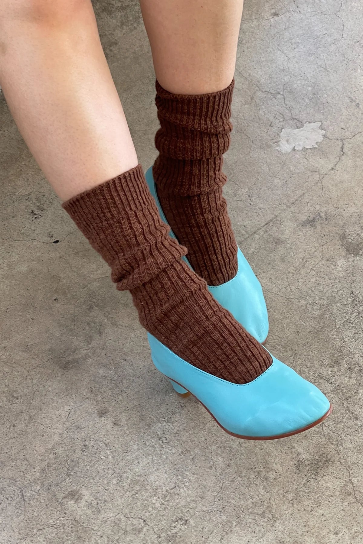Brown leg warmers over blue shoes on a concrete floor
