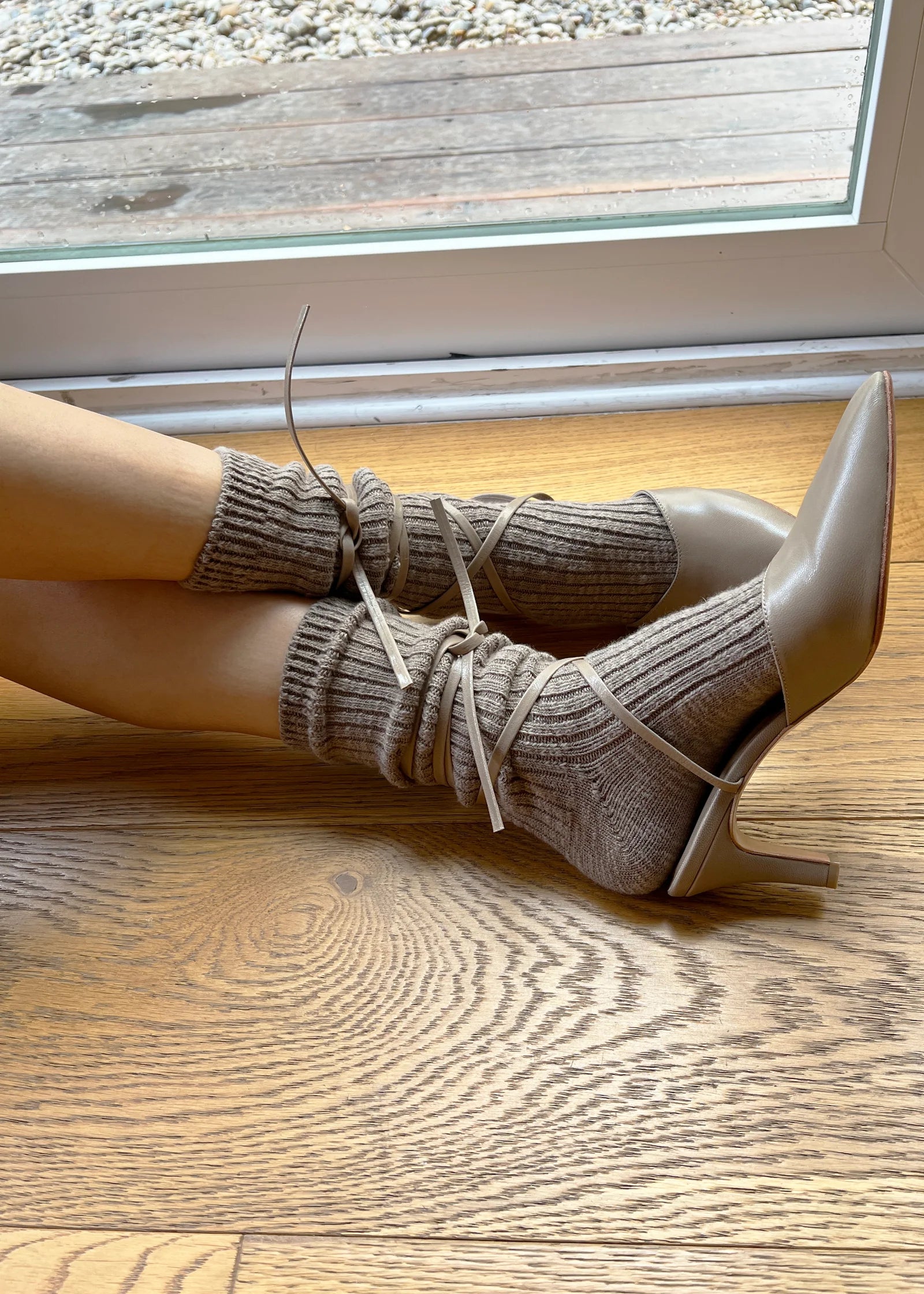White high-heeled shoes with beige ribbed socks on a wooden floor.
