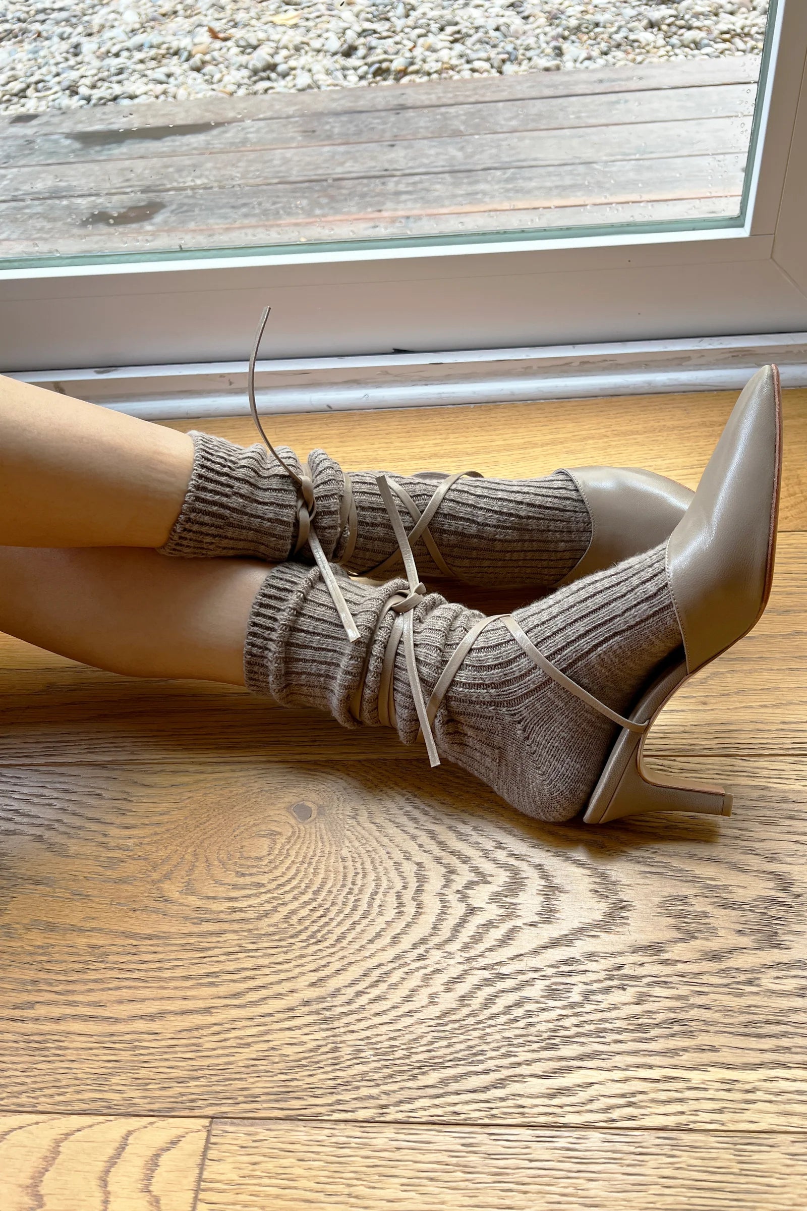 White high-heeled shoes with beige ribbed socks on a wooden floor.
