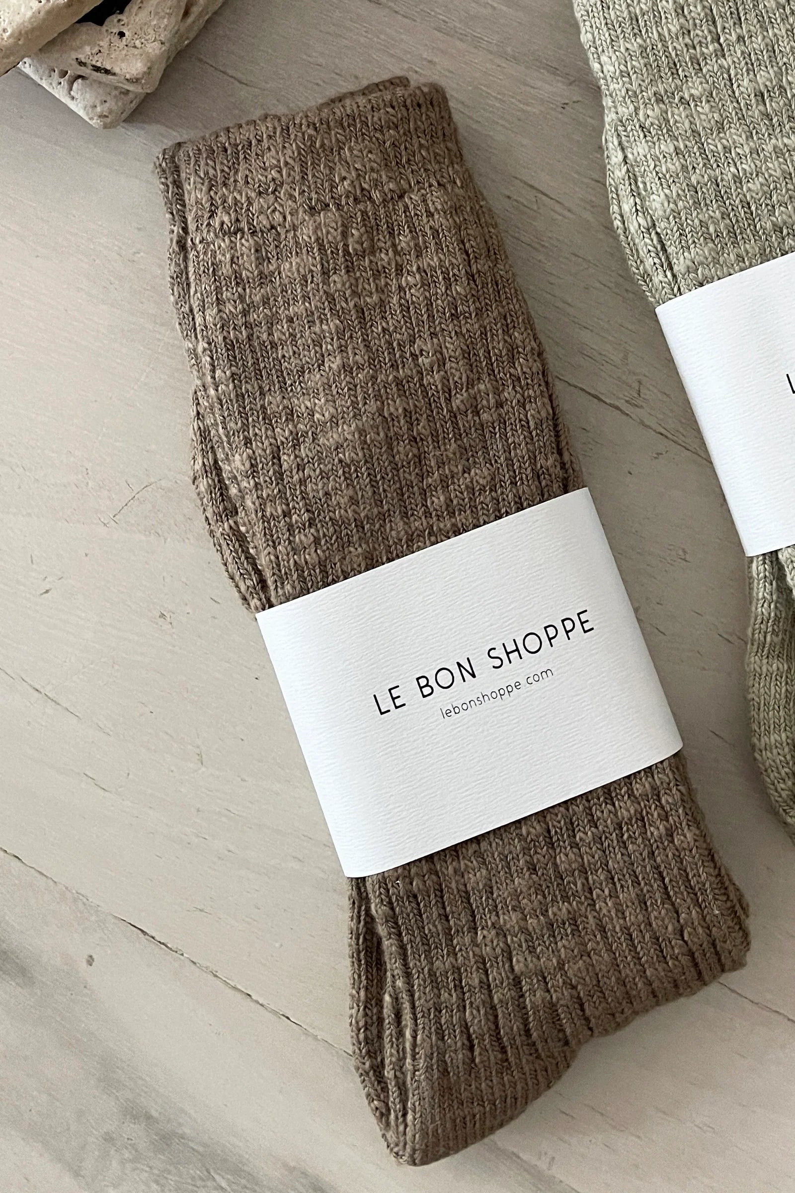 Brown sock with 'Le Bon Shoppe' label on a light wooden surface