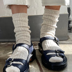 Person wearing navy sandals with white socks on a concrete floor.