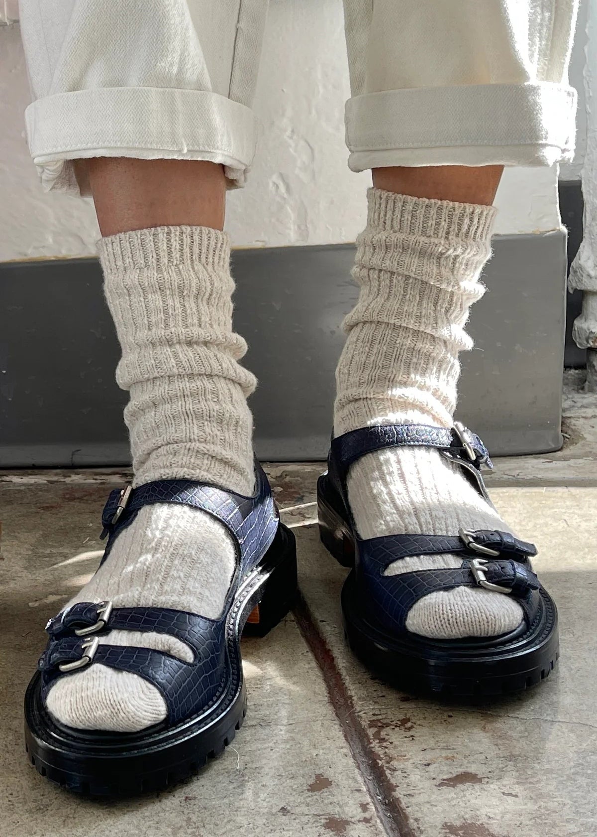 Person wearing navy sandals with white socks on a concrete floor.