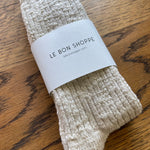 Pair of beige socks with a 'Le Bon Shoppe' label on a wooden surface