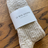 Pair of beige socks with a 'Le Bon Shoppe' label on a wooden surface