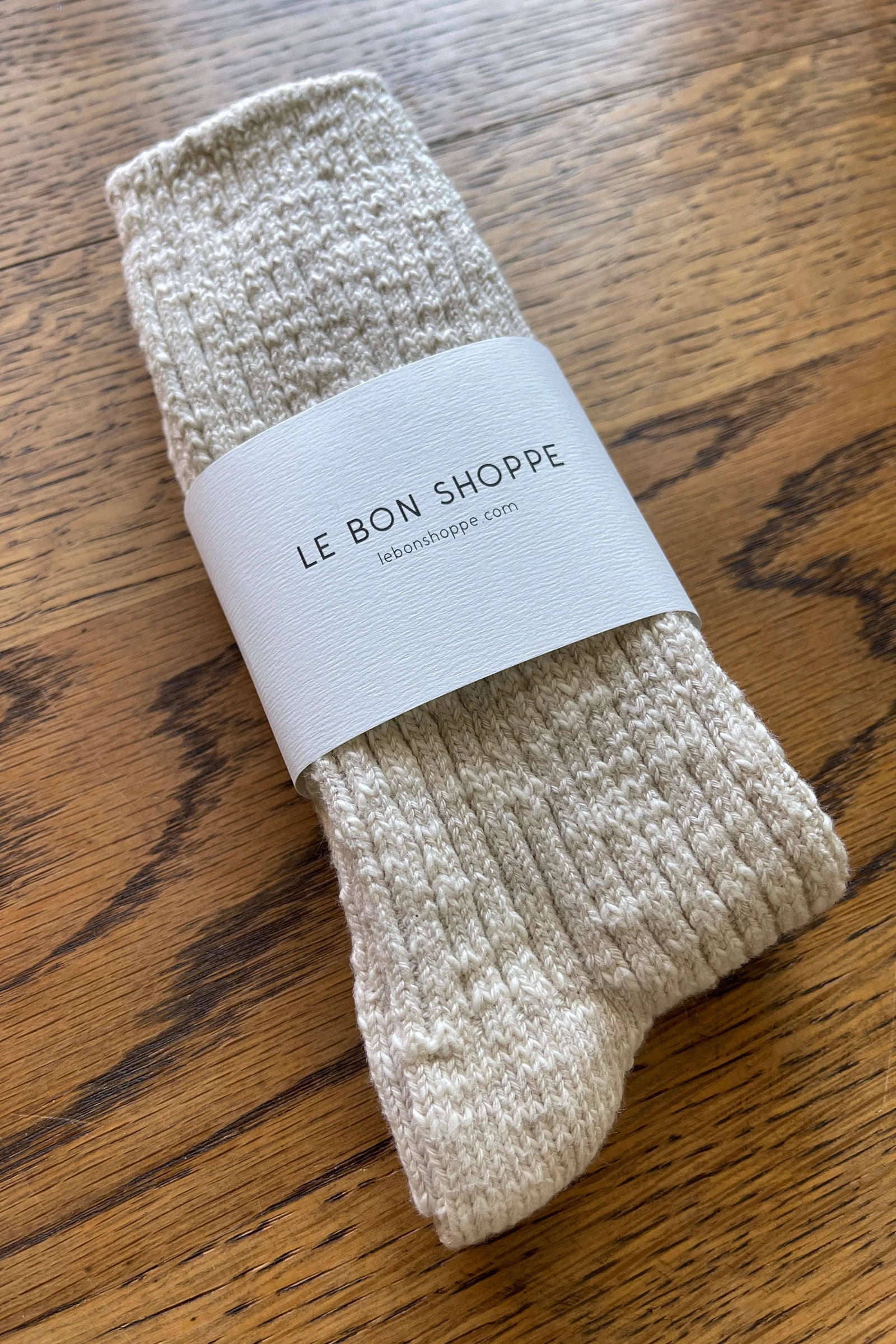 Pair of beige socks with a 'Le Bon Shoppe' label on a wooden surface