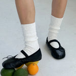Person wearing black shoes and white socks with fruits on a light gray floor.
