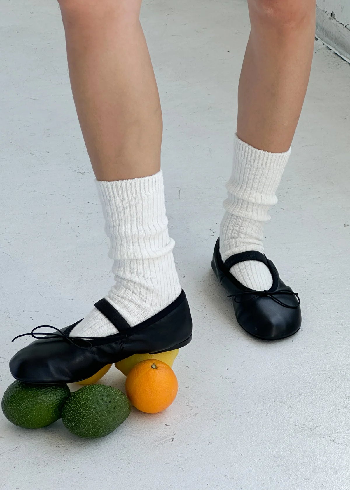Person wearing black shoes and white socks with fruits on a light gray floor.