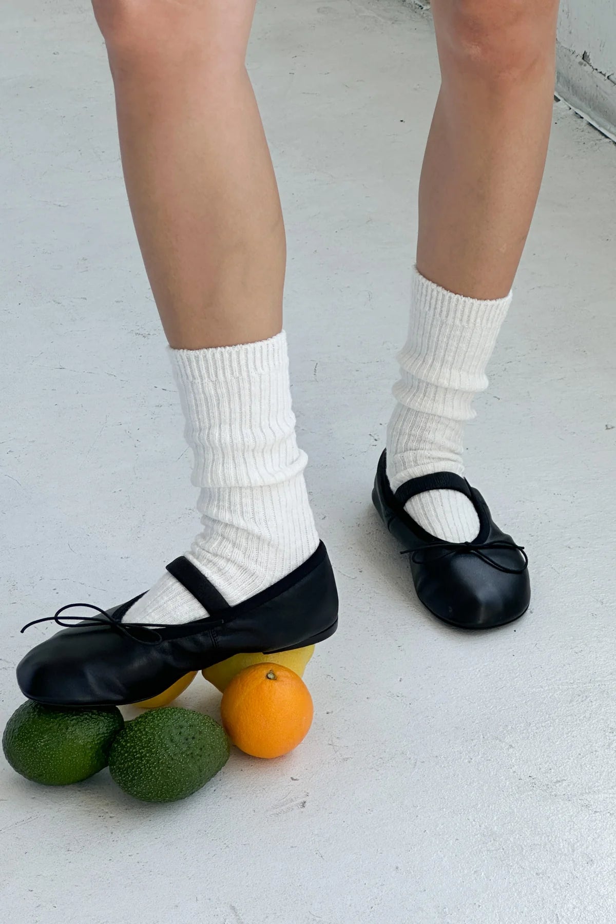 Person wearing black shoes and white socks with fruits on a light gray floor.
