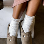 Person wearing beige suede shoes and white socks on a neutral background