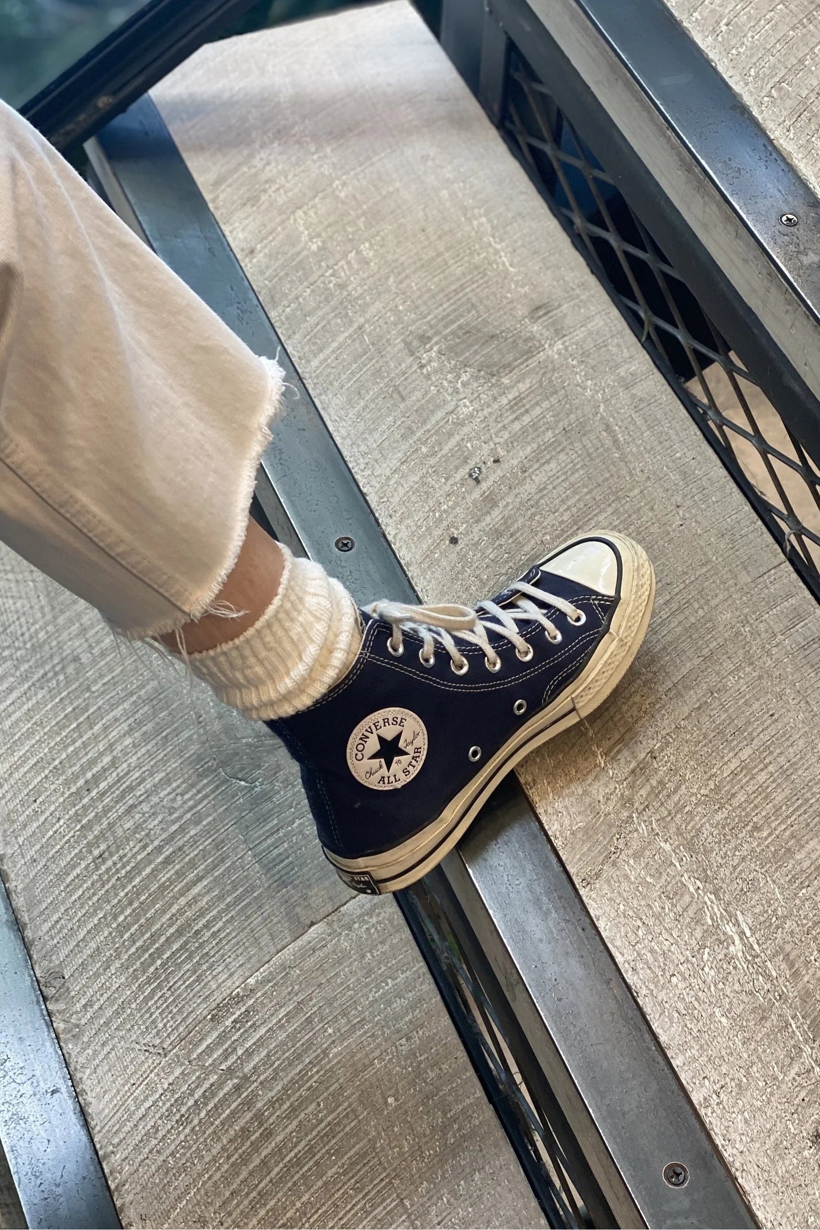Person wearing a black high-top sneaker with a white sole on a textured floor.