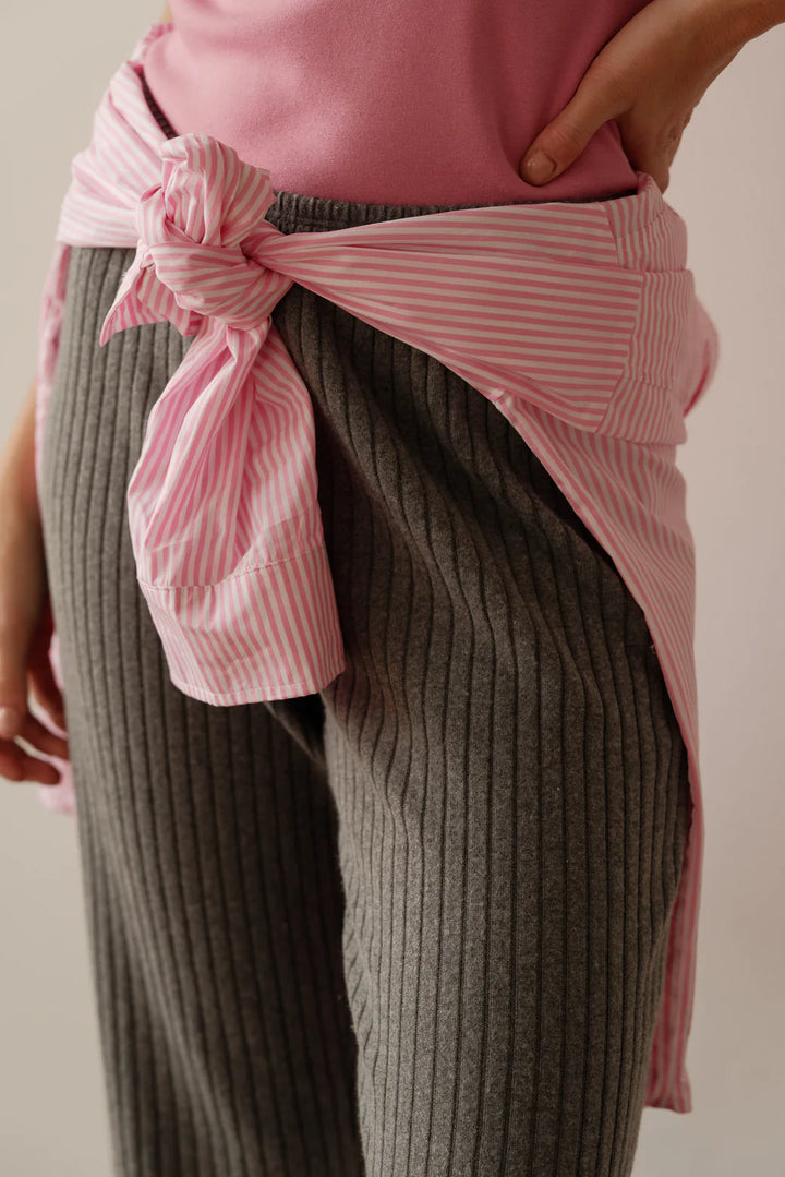 A close up detail shot of the waist of the Sweater Rib Simple Pant in Charcoal on a female model styled with a pink t-shirt tucked in and a pink striped blouse tied around her waist