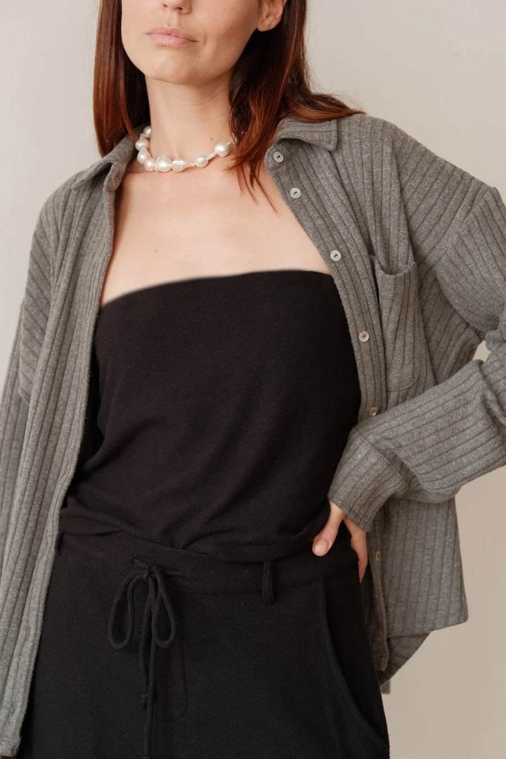 A medium shot image of a female model wearing the Sweater Rib Button Down in Charcoal Grey styled open over a black halter top and black pants