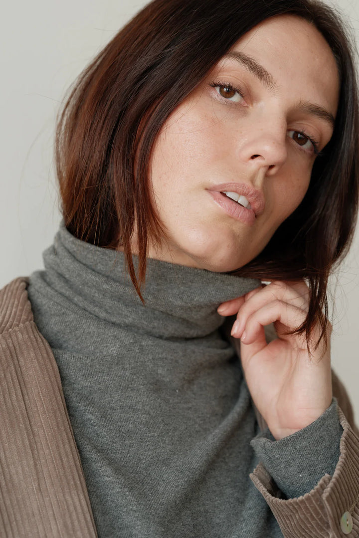 A close up image of the neckline detail of the Sweater Turtleneck in Charcoal Grey on a female model