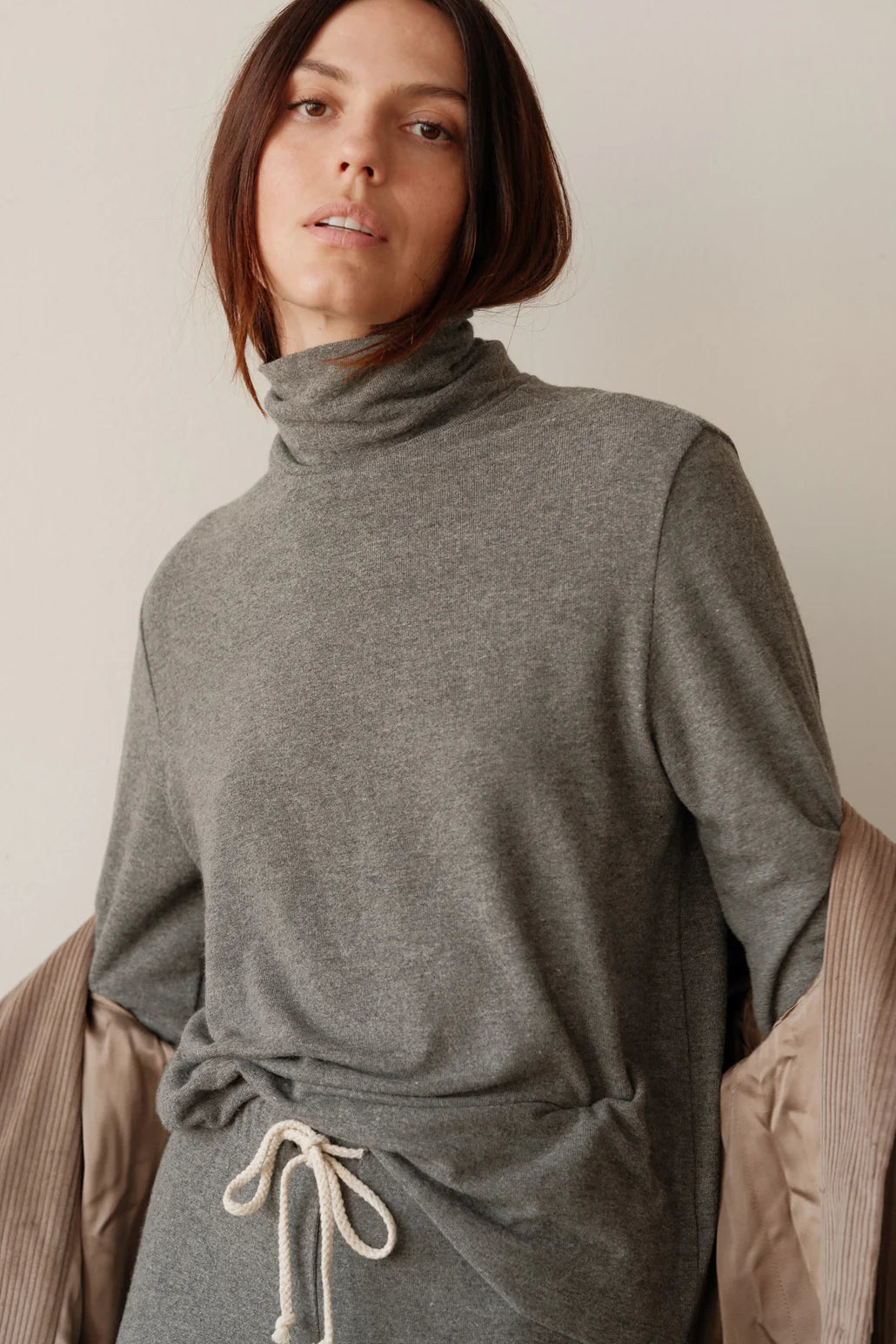 A medium close up image of a female model posing while wearing the Sweater Turtleneck in Charcoal Grey styled with a corduroy shirt draped over her arms