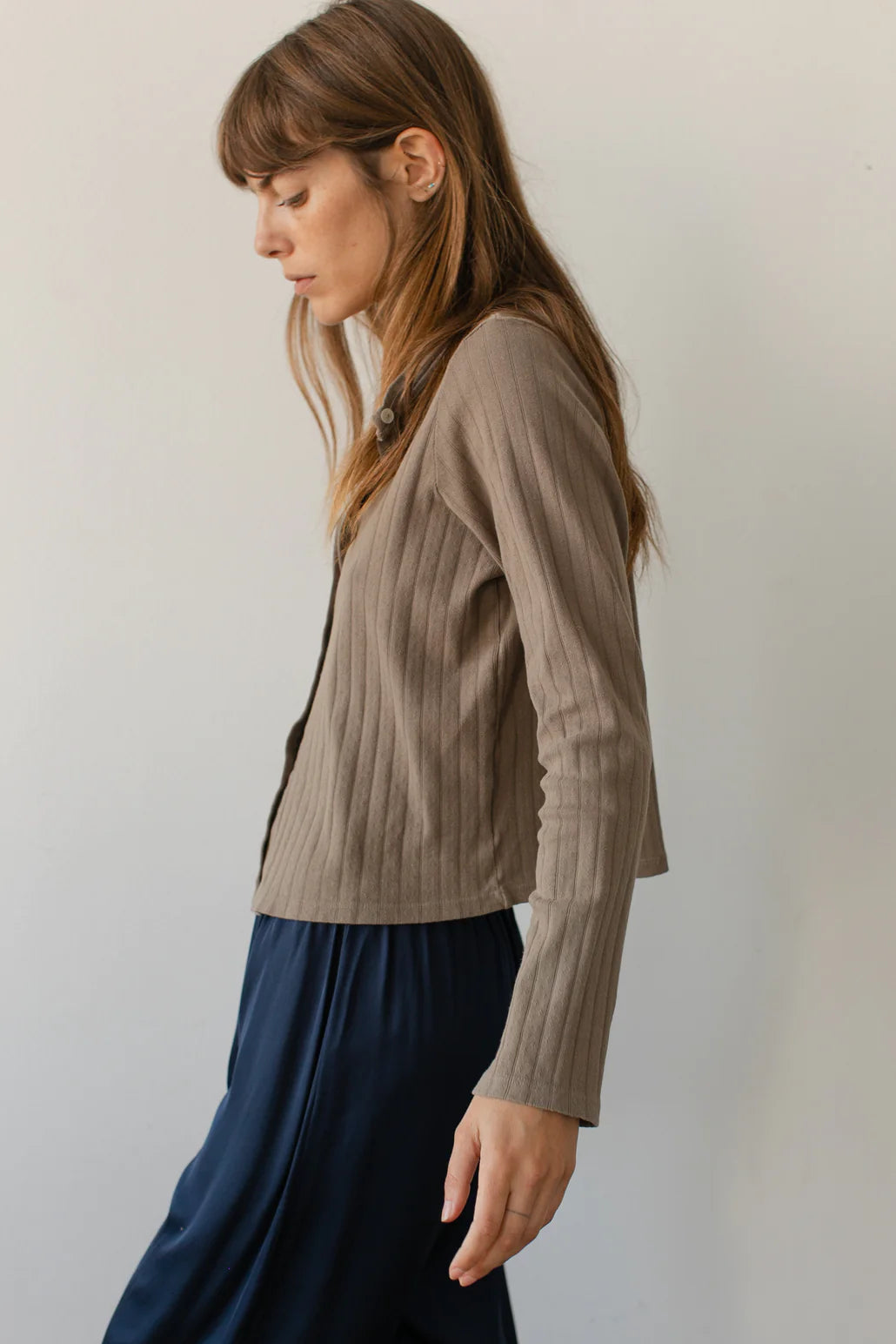 A medium shot image of the side of a female model wearing the Pointelle Cardigan styled with a navy pant